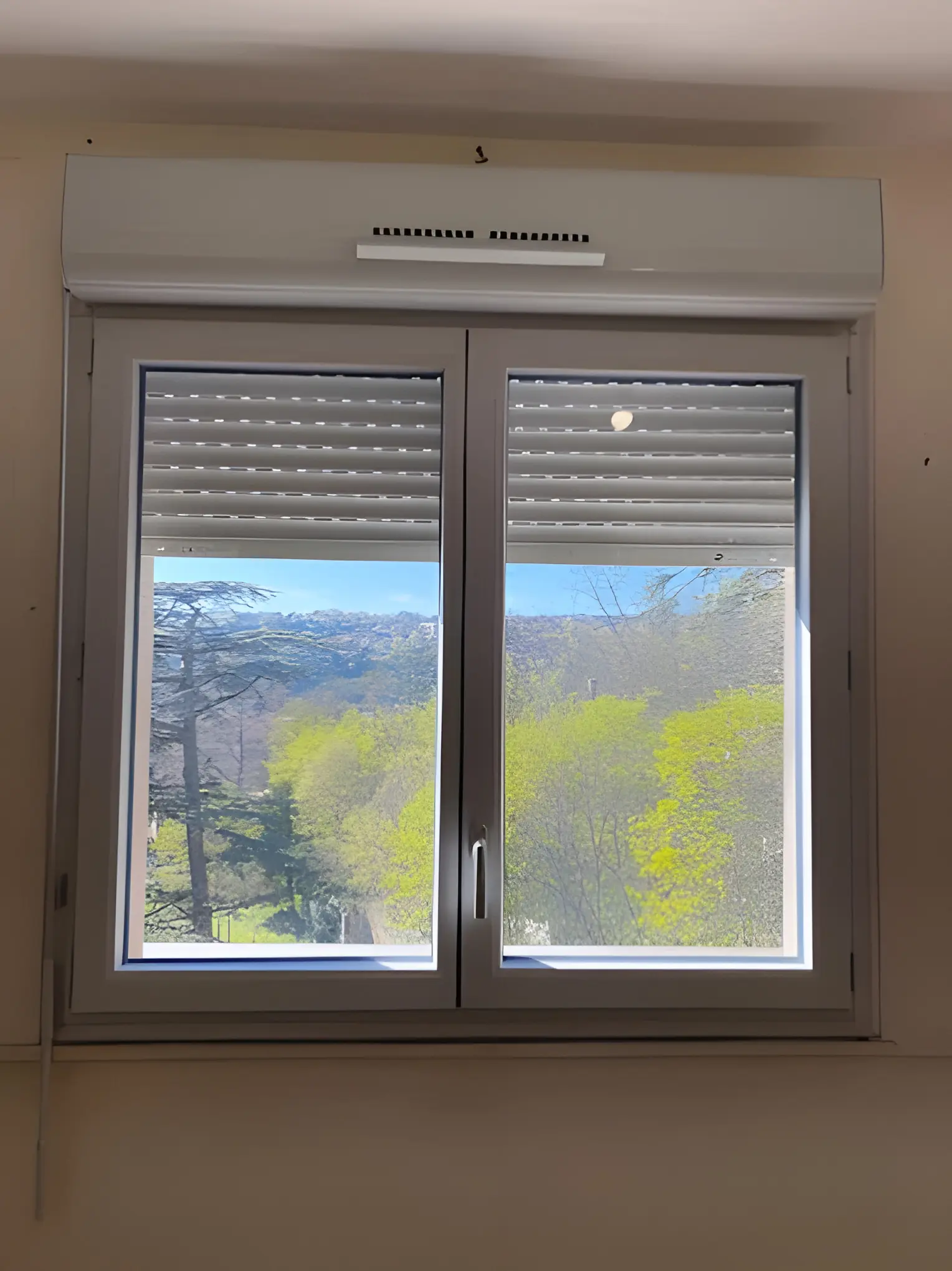 Fenêtre blanche à deux vantaux, volet roulant à demi baissé sous un coffre blanc